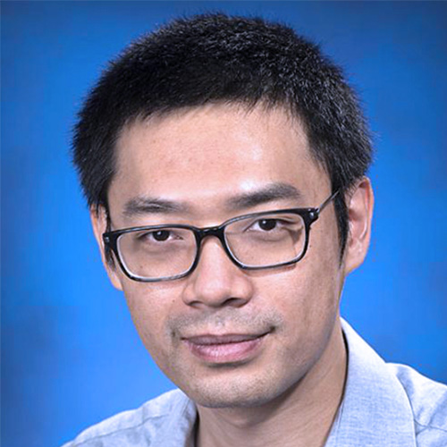 Headshot of Brookhaven researcher Yihui (Ray) Ren. He smiles and wears a light blue button up. He stands in front of a blue backdrop.