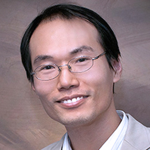 Headshot of Brookhaven researcher Shinjae Yoo. He smiles and wears a white button up with tan blazer. He wears wire frame silver glasses. He stands in front of a brown backdrop.