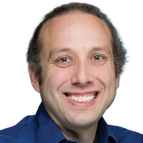 Headshot of Lawrence Livermore researcher Aaron Fisher. He smiles and wears a navy button up. He stands in front of a white backdrop.