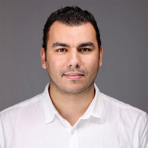 Headshot of National Renewable Energy Laboratory researcher Walid Arsalane. He smiles and wears a white button up. He stands in front of a gray backdrop.