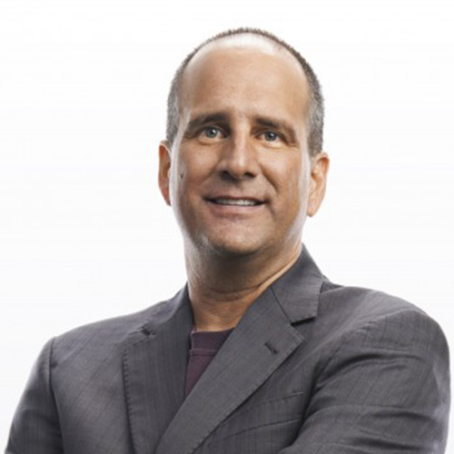 Headshot of AMD speaker Brad McCredie. He smiles and wears a dark gray blazer with a plum button-up. He stands in front of a white backdrop.